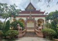 Back view of the vihara at Wat Bo pagoda in Siem Reap, showing a decorative archway with two gajasimha statues, stairway and lush green trees around the temple