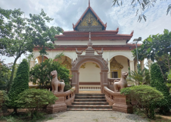 Back view of the vihara at Wat Bo pagoda in Siem Reap, showing a decorative archway with two gajasimha statues, stairway and lush green trees around the temple