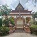 Back view of the vihara at Wat Bo pagoda in Siem Reap, showing a decorative archway with two gajasimha statues, stairway and lush green trees around the temple