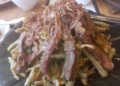 Close-up of Cambodian morning glory salad at Kraya Angkor Restaurant in Phnom Penh, featuring crispy battered morning glory topped with sliced grilled beef and golden fried shallots on a dark plate.