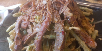 Close-up of Cambodian morning glory salad at Kraya Angkor Restaurant in Phnom Penh, featuring crispy battered morning glory topped with sliced grilled beef and golden fried shallots on a dark plate.
