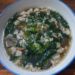 Homemade Cambodian soup in a white bowl, filled with minced pork, ivy gourd leaves, dried shrimp, and mushrooms in a clear broth on a wooden table