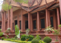 Red sandstone-style National Museum of Cambodia building with ornate Khmer roof, columns, and landscaped garden in front