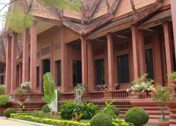Red sandstone-style National Museum of Cambodia building with ornate Khmer roof, columns, and landscaped garden in front