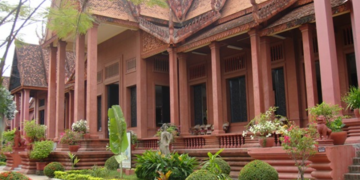 Red sandstone-style National Museum of Cambodia building with ornate Khmer roof, columns, and landscaped garden in front