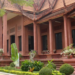 Red sandstone-style National Museum of Cambodia building with ornate Khmer roof, columns, and landscaped garden in front