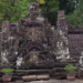 Stone naga friezes and weathered carvings at Neak Poan temple in Angkor, framed by laterite steps, potted plants, and the green edge of the surrounding baray.
