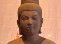 Sandstone 7th‑century Devi statue from Sambor Prei Kuk style, showing elegant Khmer feminine form with high jata hairstyle and sampot, displayed against a warm backdrop.