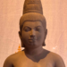 Sandstone 7th‑century Devi statue from Sambor Prei Kuk style, showing elegant Khmer feminine form with high jata hairstyle and sampot, displayed against a warm backdrop.