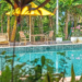 Outdoor swimming pool at Sanssouci Kep surrounded by tropical plants, bamboo loungers, and yellow umbrellas in a lush garden setting