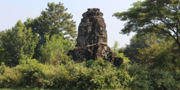 Overgrown four-faced Angkorian tower of Banteay Chhmar reflected in a tranquil baray, with Bayon-style smiling faces from the era of Jayavarman VII framed by lush Cambodian greenery.