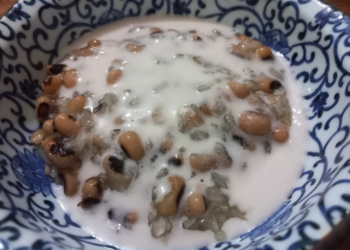 Close-up of a Cambodian dessert with black-eyed peas and sticky rice covered in creamy coconut milk, served in a blue-and-white patterned ceramic bowl.