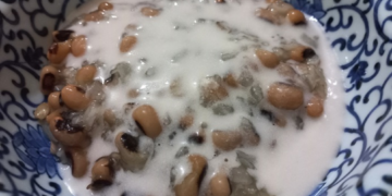 Close-up of a Cambodian dessert with black-eyed peas and sticky rice covered in creamy coconut milk, served in a blue-and-white patterned ceramic bowl.