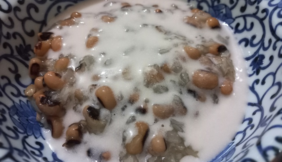 Close-up of a Cambodian dessert with black-eyed peas and sticky rice covered in creamy coconut milk, served in a blue-and-white patterned ceramic bowl.