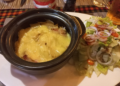 Close-up of tarticlette at La Guinguette de Siem Reap, a French-style potato, bacon, onion and raclette cheese gratin served in a black dish with green salad on the side in Siem Reap, Cambodia.
