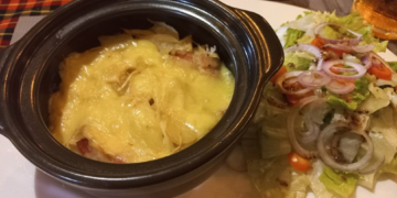 Close-up of tarticlette at La Guinguette de Siem Reap, a French-style potato, bacon, onion and raclette cheese gratin served in a black dish with green salad on the side in Siem Reap, Cambodia.