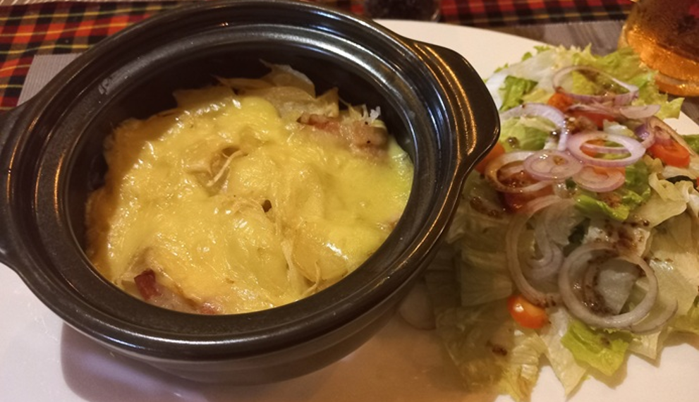 Close-up of tarticlette at La Guinguette de Siem Reap, a French-style potato, bacon, onion and raclette cheese gratin served in a black dish with green salad on the side in Siem Reap, Cambodia.
