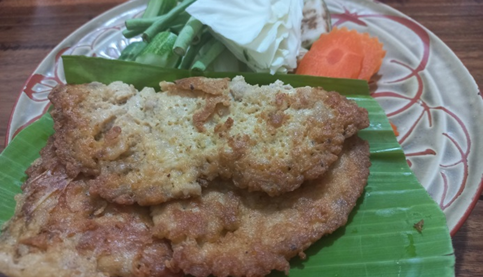 Cambodian omelette made with trei proma salted semi-dried fish, served on banana leaf with cabbage, long beans, okra, eggplant and carrot on a patterned plate.