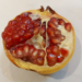 Half-opened pomegranate on a white surface, showing glossy red seeds and pale rind, photographed in natural Cambodian indoor light.