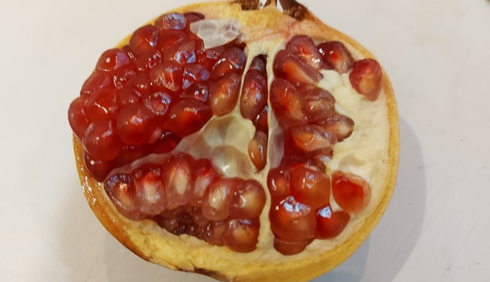 Half-opened pomegranate on a white surface, showing glossy red seeds and pale rind, photographed in natural Cambodian indoor light.