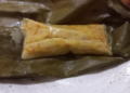 Close up of Cambodian num lpov steamed pumpkin cake unwrapped from a banana leaf, showing its soft golden pumpkin filling and glossy coconut rice exterior on a plate.