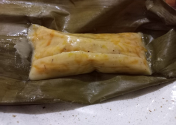Close up of Cambodian num lpov steamed pumpkin cake unwrapped from a banana leaf, showing its soft golden pumpkin filling and glossy coconut rice exterior on a plate.