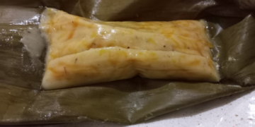 Close up of Cambodian num lpov steamed pumpkin cake unwrapped from a banana leaf, showing its soft golden pumpkin filling and glossy coconut rice exterior on a plate.