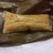 Close up of Cambodian num lpov steamed pumpkin cake unwrapped from a banana leaf, showing its soft golden pumpkin filling and glossy coconut rice exterior on a plate.