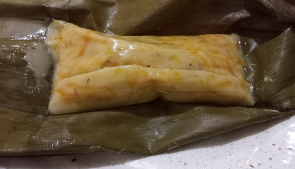 Close up of Cambodian num lpov steamed pumpkin cake unwrapped from a banana leaf, showing its soft golden pumpkin filling and glossy coconut rice exterior on a plate.