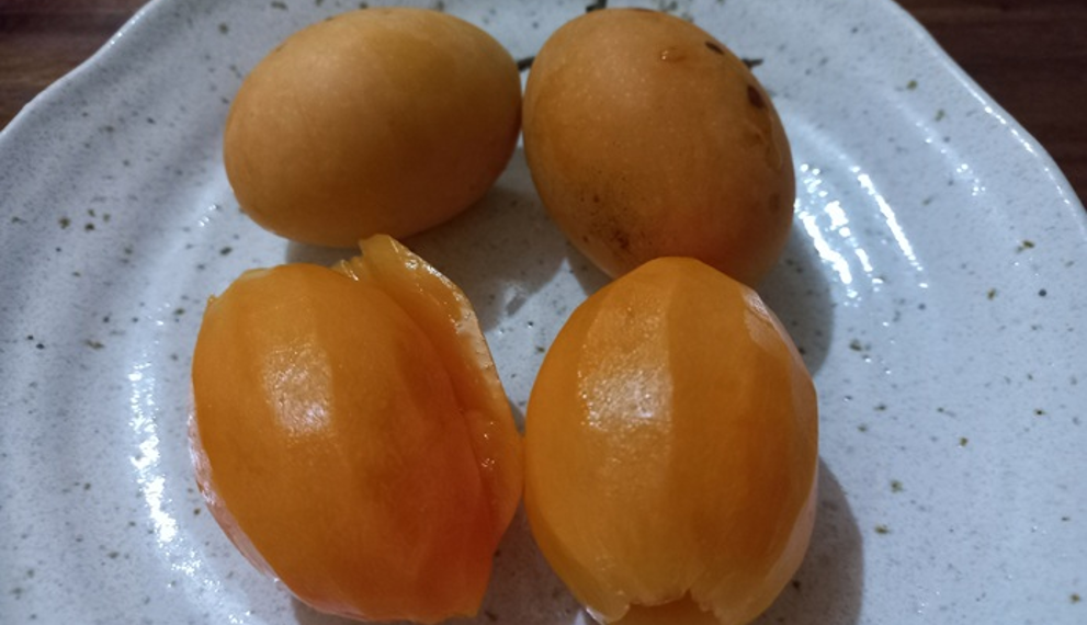Four ripe marian plums, two peeled and two whole, on a speckled ceramic plate on a wooden table, illustrating Cambodian home-style fruit enjoyment.