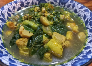 Close up of a bowl of samla prahae, traditional Cambodian vegetable meat soup with pumpkin, leafy greens and fermented fish in a clear lemongrass broth.