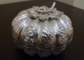 Close-up of a finely chased Khmer silver pumpkin-shaped betel nut box from Cambodia, with intricate floral and scroll repoussé patterns on a dark wooden surface.