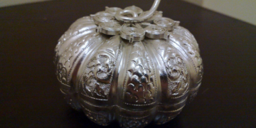 Close-up of a finely chased Khmer silver pumpkin-shaped betel nut box from Cambodia, with intricate floral and scroll repoussé patterns on a dark wooden surface.