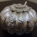 Close-up of a finely chased Khmer silver pumpkin-shaped betel nut box from Cambodia, with intricate floral and scroll repoussé patterns on a dark wooden surface.