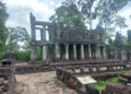 Two storied stone pavilion with round columns at Preah Khan temple in Angkor, surrounded by lush trees and ancient terraces, Siem Reap, Cambodia.
