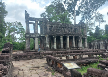 Two storied stone pavilion with round columns at Preah Khan temple in Angkor, surrounded by lush trees and ancient terraces, Siem Reap, Cambodia.