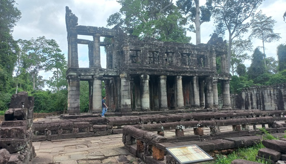 Two storied stone pavilion with round columns at Preah Khan temple in Angkor, surrounded by lush trees and ancient terraces, Siem Reap, Cambodia.