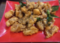 Close up of deep-fried beef tendon pieces on a red plate, sprinkled with sesame seeds and garnished with fried kaffir lime leaves at a small street side restaurant in Kampong Thom, Cambodia.