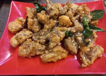 Close up of deep-fried beef tendon pieces on a red plate, sprinkled with sesame seeds and garnished with fried kaffir lime leaves at a small street side restaurant in Kampong Thom, Cambodia.