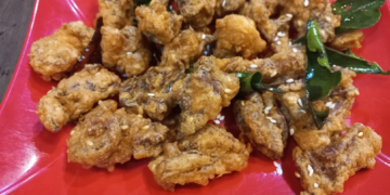 Close up of deep-fried beef tendon pieces on a red plate, sprinkled with sesame seeds and garnished with fried kaffir lime leaves at a small street side restaurant in Kampong Thom, Cambodia.