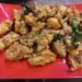 Close up of deep-fried beef tendon pieces on a red plate, sprinkled with sesame seeds and garnished with fried kaffir lime leaves at a small street side restaurant in Kampong Thom, Cambodia.