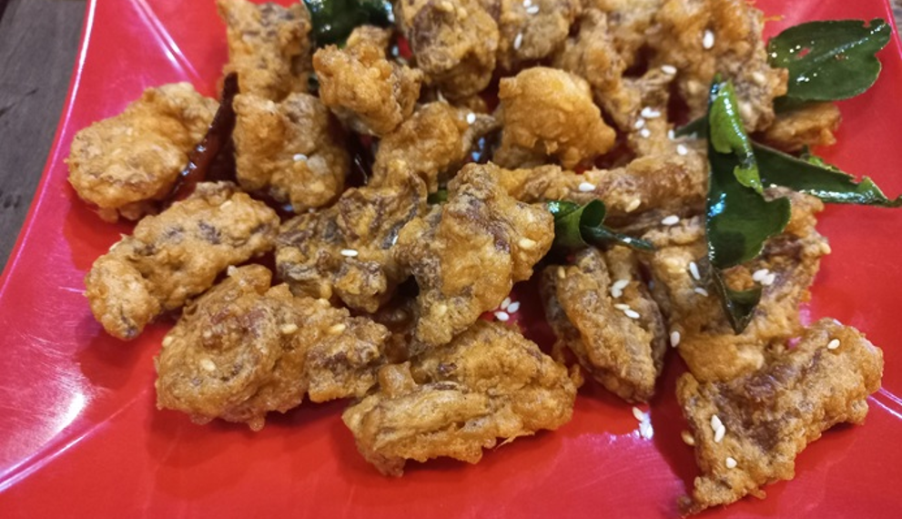 Close up of deep-fried beef tendon pieces on a red plate, sprinkled with sesame seeds and garnished with fried kaffir lime leaves at a small street side restaurant in Kampong Thom, Cambodia.