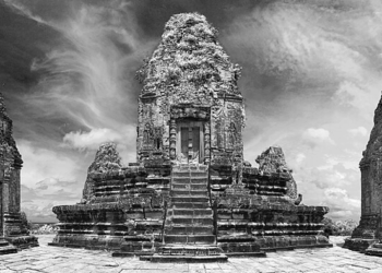Black‑and‑white panoramic view of Pre Rup’s upper terrace at Angkor, showing the central stepped sandstone prasat flanked by two smaller brick towers under a dramatic cloudy sky.