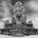 Black‑and‑white panoramic view of Pre Rup’s upper terrace at Angkor, showing the central stepped sandstone prasat flanked by two smaller brick towers under a dramatic cloudy sky.