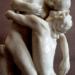 Marble sculpture Shakuntala by Camille Claudel showing two nude lovers locked in a tender embrace, inspired by Kalidasa’s Sanskrit play, against a neutral museum background.