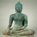 Fourteenth century Sukhothai bronze Buddha statue seated cross-legged in meditation, right hand resting on knee, left hand in lap, with flame-like finial on top of the head.