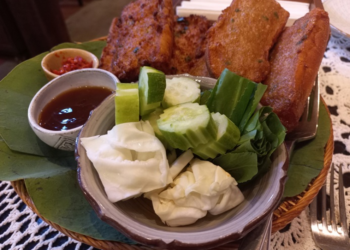 Crispy Cambodian fried bread topped with pork and fish cake, served with cucumber, cabbage, herbs and dipping sauces on a leaf lined tray at Maedy restaurant in Siem Reap.