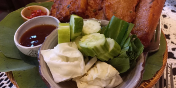 Crispy Cambodian fried bread topped with pork and fish cake, served with cucumber, cabbage, herbs and dipping sauces on a leaf lined tray at Maedy restaurant in Siem Reap.