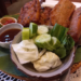 Crispy Cambodian fried bread topped with pork and fish cake, served with cucumber, cabbage, herbs and dipping sauces on a leaf lined tray at Maedy restaurant in Siem Reap.