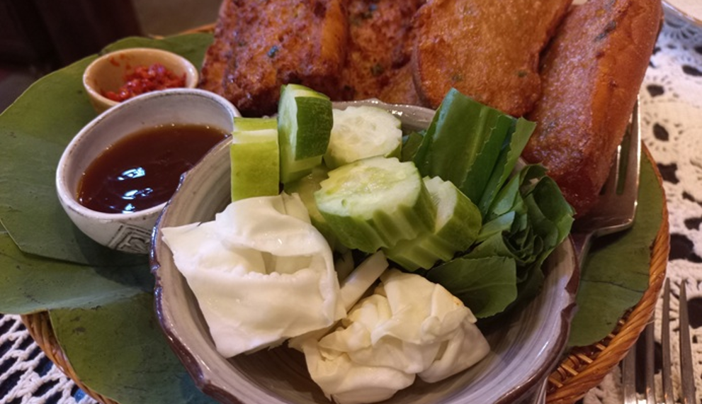 Crispy Cambodian fried bread topped with pork and fish cake, served with cucumber, cabbage, herbs and dipping sauces on a leaf lined tray at Maedy restaurant in Siem Reap.